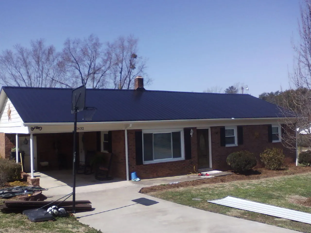 Finished dark blue metal roof on a brick ranch with a carport in Rochester