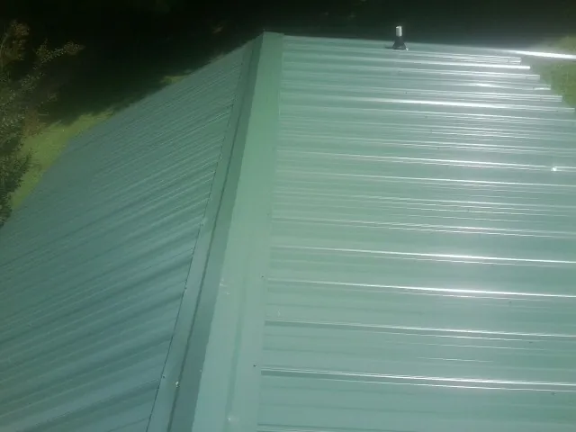 New green metal panels meeting at the ridge of a roof — Flat Roof Repair work by our crew in Rochester