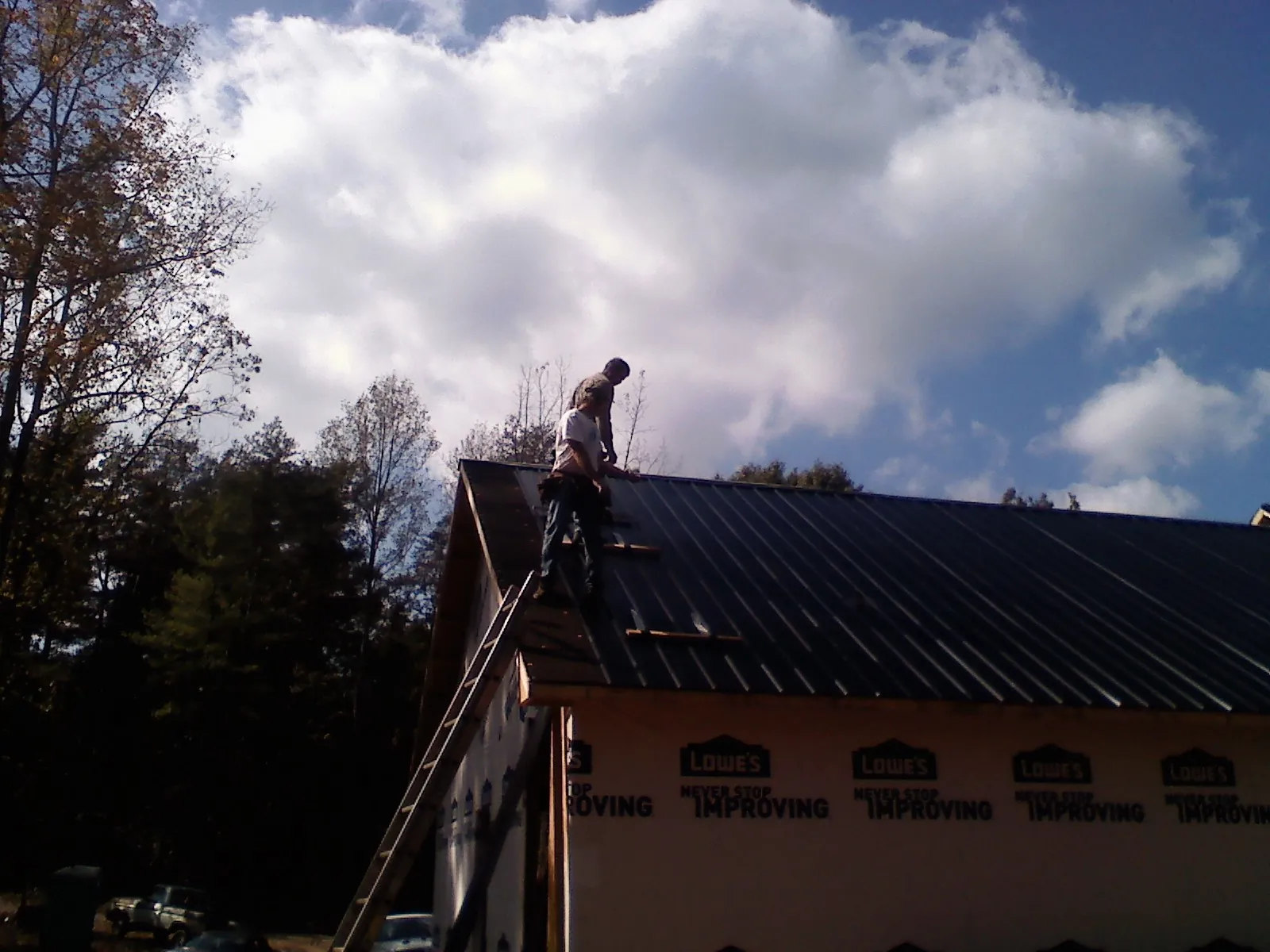 Roofer fastening dark metal panels high against a cloudy sky, from a Roof Inspection job in Rochester